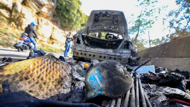 A burned press helmet is seen next to a destroyed vehicle