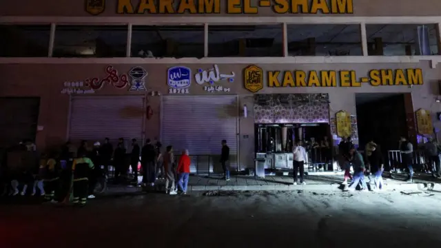 A large crowd stands next to several shuttered shop fronts