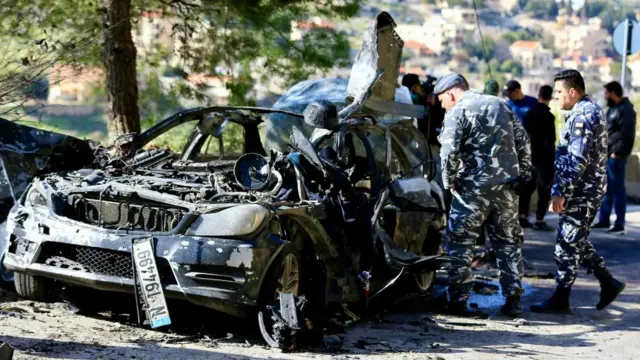 Policemen inspect a destroyed vehicle that has been completely burnt up after being hit by an Israeli strike