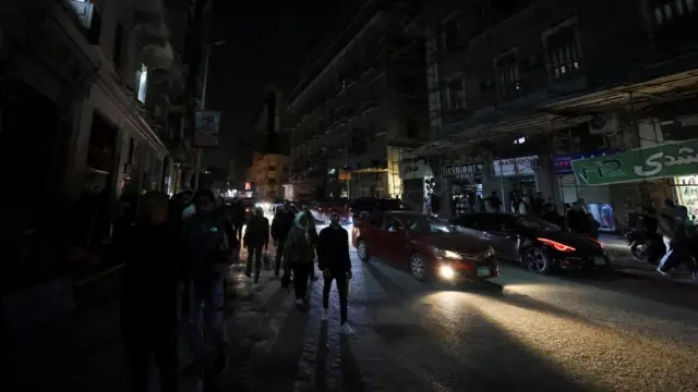 Crowds walk down a dark street in Cairo only lit up by the lights of cars