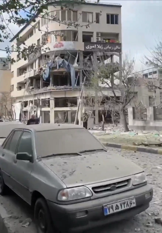 Building hit by strike seen in the background of the picture. Interior of the building appears largely destroyed, while the overall structure is still standing.