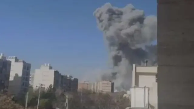A large smoke plume rises into the air in the middle of an urban area