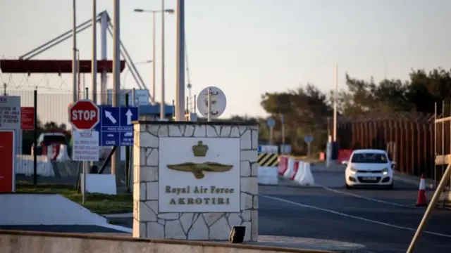 A landscape image of the entrance to RAF Akrotiri - a sign reads 'Royal Air Force Akrotiri' and a white car is in the background
