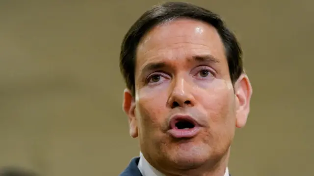 Close up of Rubio speaking in front of a beige background