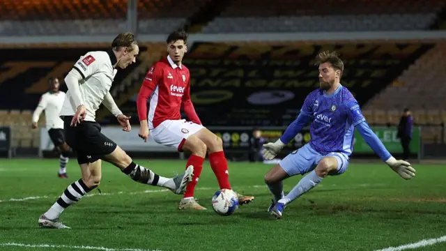 Ben Waine (left) swings his leg out after kicking the ball as Joe Lumley (left) crouches with his arms out wide to make a save