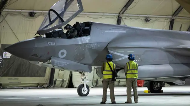 A grey plan with two workers standing by it in high-vis