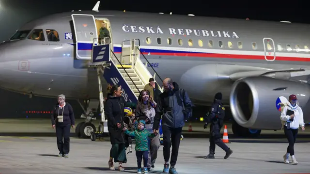 A family holds hands on the tarmac of a runway with a Czech plane in the background