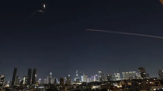 Trails of light in the night sky above skyscrapers