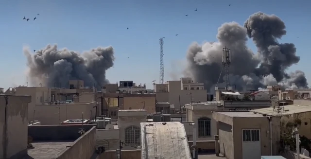 A screengrab of a video showing several large smoke plumes rising over multi-storey buildings