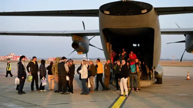 A group of people stand on the tarmac of an airport under a plane