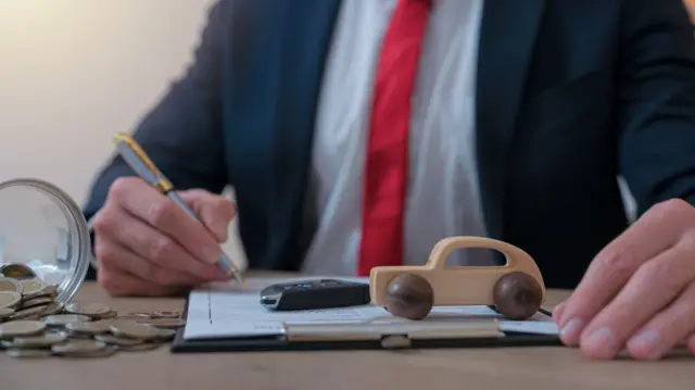 Stock image of car dealer signing a contract for the purchase or leasing of a new car. New car keys and toy car in foreground.