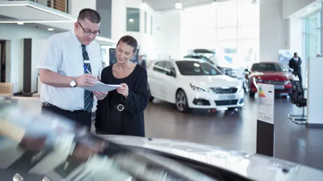 Stock photo of a car seller and customer looking over paperwork in a car dealership.