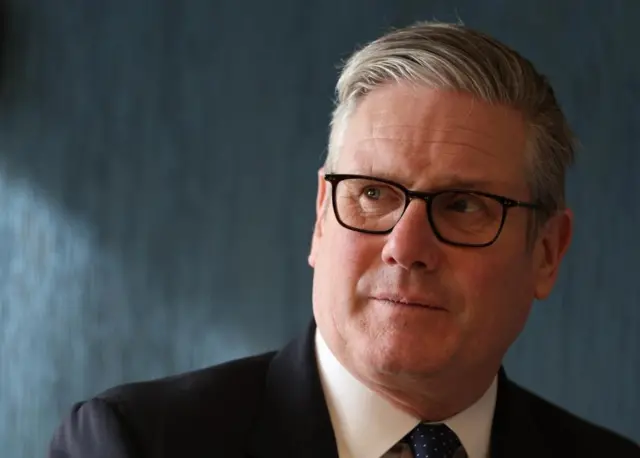 Prime Minister Sir Keir Starmer pictured wearing glasses. He is wearing a black suit jacket and navy tie.