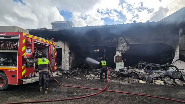 Two firefighters can be seen with hoses spraying a building that has been turned black by an Israeli airstrike