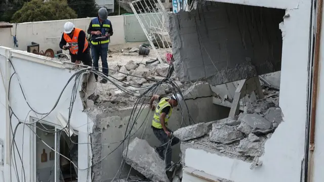 Workers climb through a building that has been damaged, with some walls crumbling and wires hanging assess damage after an Iranian strike in Haifa, Israel