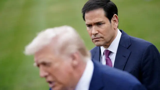 US Secretary of State Marco Rubio stands behind an out of focus Donald Trump on the White House lawn.