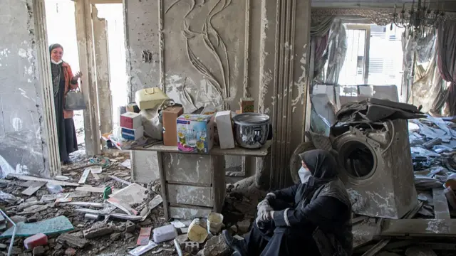Residents sit amid debris in a residential building that was hit in an airstrike earlier this morning on March 30, 2026 in the west of Tehran, Iran.