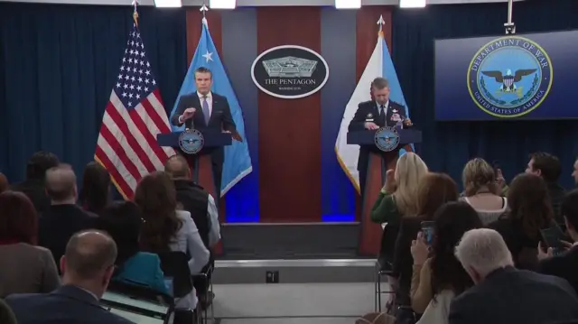 US Defence Secretary Pete Hegseth (left) and chairman of the Joint Chiefs of Staff, General Dan Caine (right) giving a briefing at the Pentagon with journalists sat in front of them and flags behind them, including the US flag