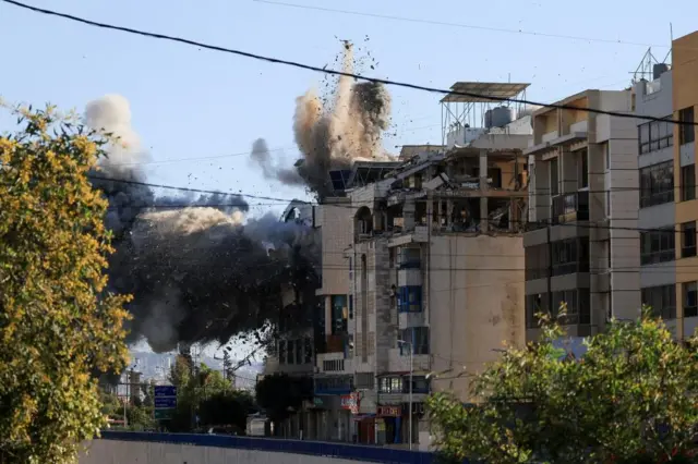 A large cloud of smoke billows from the top floor of a multi-level residential building, in what appears to be the moment of impact from a missile strike. Smoke and debris are also flying upwards.
