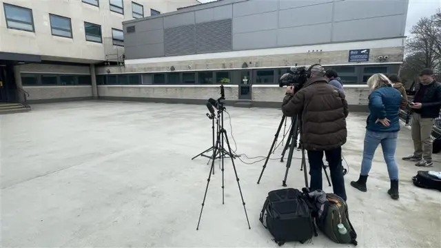Journalists and a couple of camera tripods are set up, facing the concrete building of Chelmsford police station