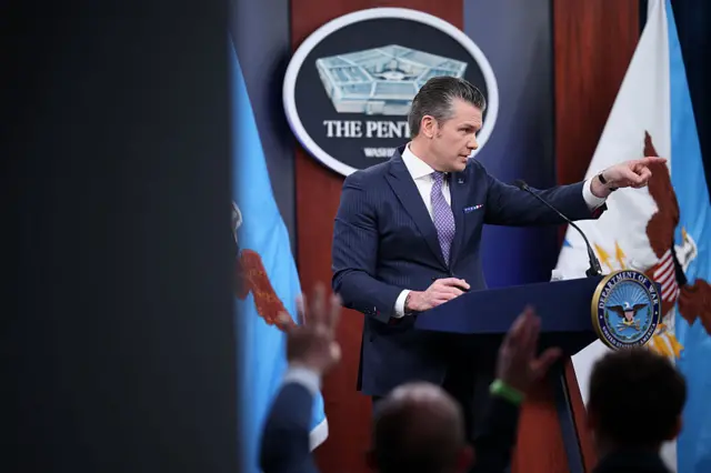 US Defence Secretary pointing at a journalist in a crowd in front of him in the Pentagon briefing room, as journalists in the foreground are blurry and have their hands up