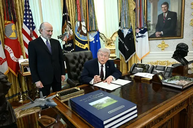 US President Donald Trump sits behind his desk in the Oval Office with Commerce Secretary Howard Lutnick standing next to him