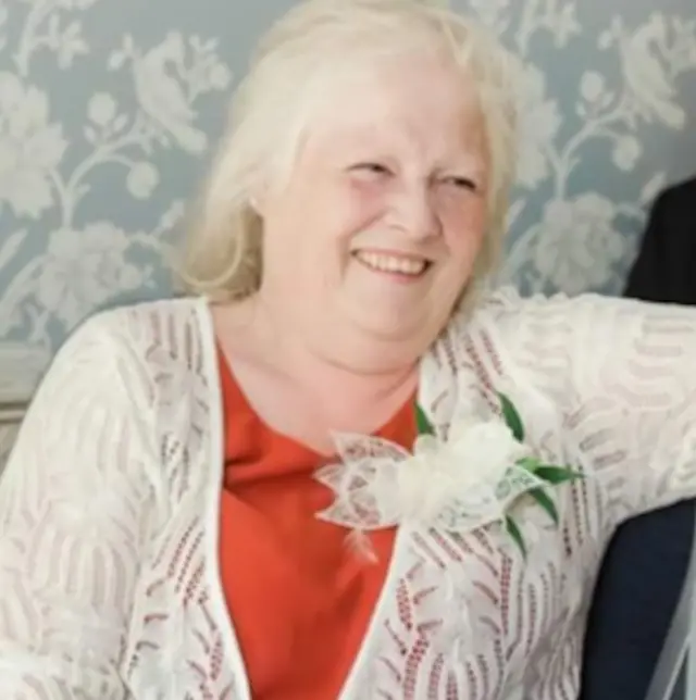 Esther Martin smiling to the right of the camera wearing an orange T-shirt and white cardigan
