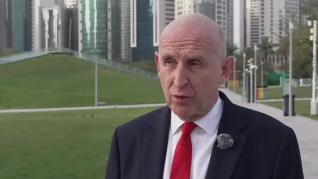 Head shot of Healey talking in front of skyscrapers and a park