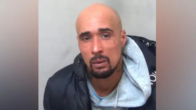 A police custody photo of Ashley Warren, who is wearing a grey hoodie and a black coat over the top