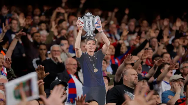 Fans hold aloft a cardboard cutout of Oliver Glasner holding the FA Cup trophy