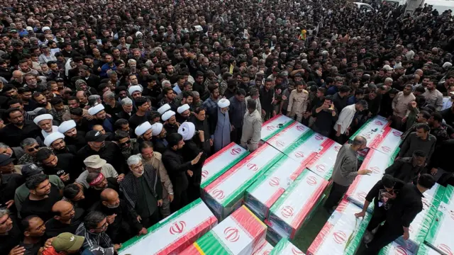Coffins wrapped in the Iranian flag are surrounded by a mass of people.