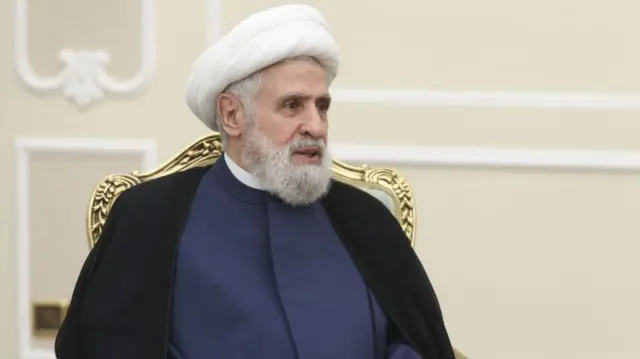 Naim Qassem sitting on a gilded chair and speaking