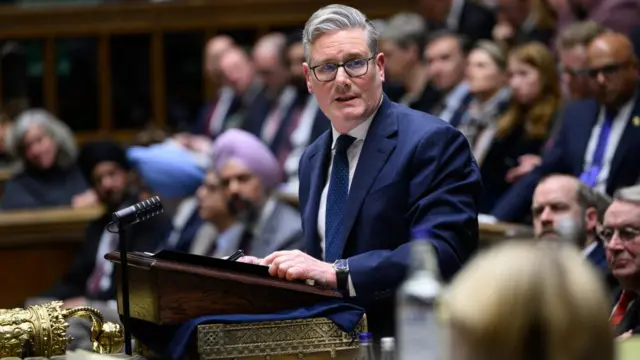 Starmer in the Commons standing at a lectern speaking as he looks to the side of him. There's rows of people sat behind him looking at him keenly