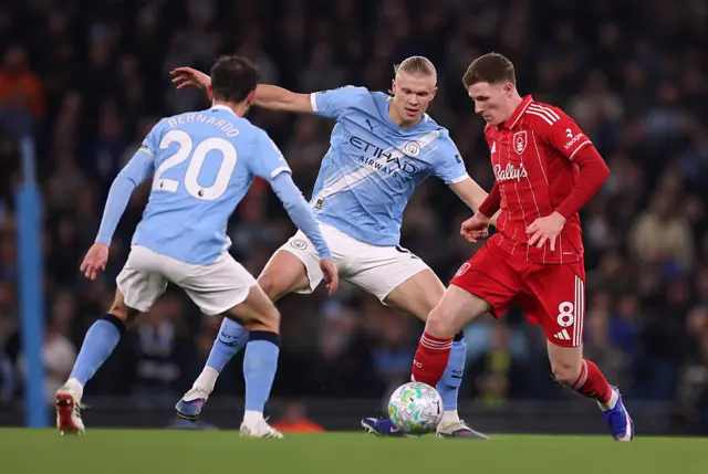 Elliot Anderson of Nottingham Forest is challenged by Bernardo Silva and Erling Haaland of Manchester City