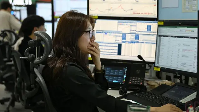 A woman puts her hand over her mouth as she reacts to stock market figures on a screen