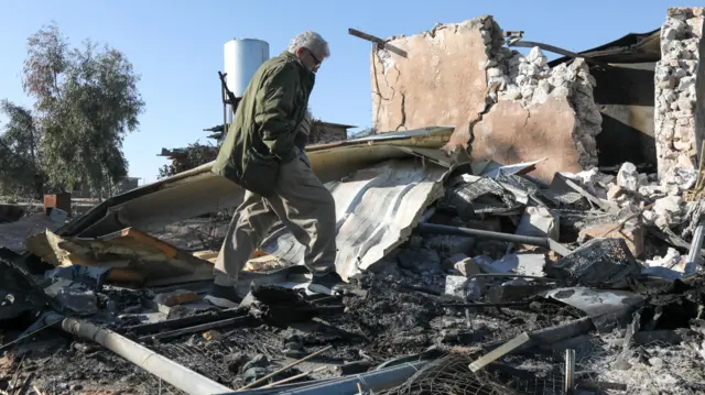 A man walks through debris of a crumbled building.