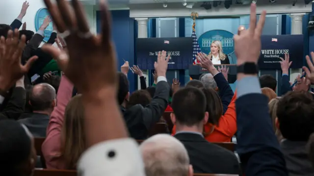 Reporters raise hands in the air to ask questions of Karoline Leavitt