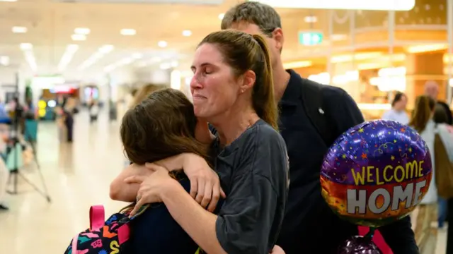 A woman hugs a young child as she holds a welcome home balloon