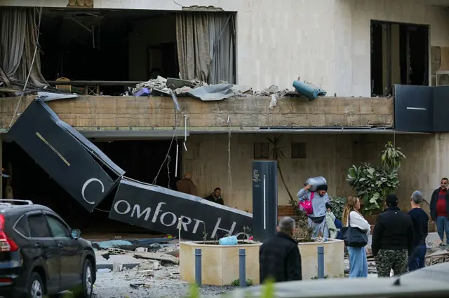 People stand outside a hotel, which was damaged in an Israeli air strike
