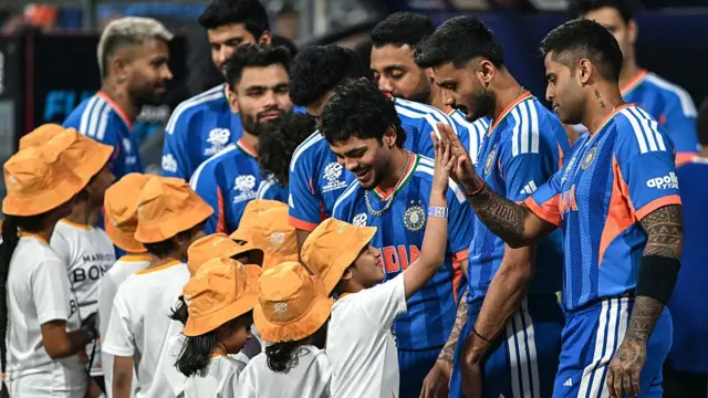 India's captain Suryakumar Yadav (R) and his teammates Axar Patel (2R) and Ishan Kishan (3R) interact with children as they arrive for their national anthem before the start of the 2026 ICC Men's T20 Cricket World Cup semi-final match between India and England at the Wankhede Stadium in Mumbai on