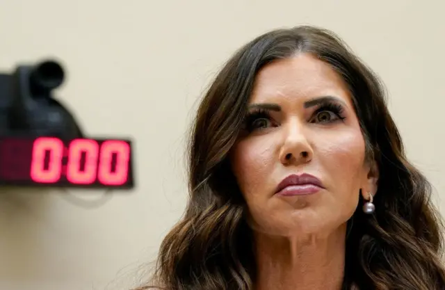 A close-up of Kristi Noem with red digital zeroes on the wall behind her