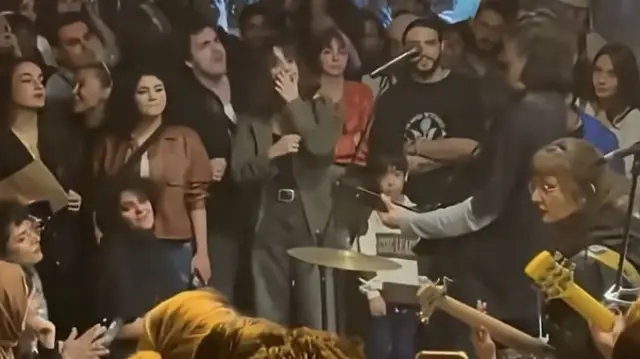 a rock band is surrounded by fans. they play guitars and drums
