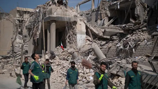 a group of men wearing matching vests and carrying tools walk through the debris of a destroyed building