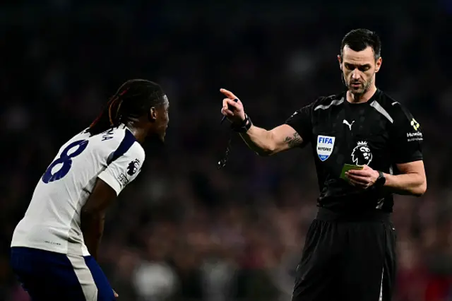 Referee Andy Madley shows a yellow card to Tottenham Hotspur's Malian midfielder #08 Yves Bissouma
