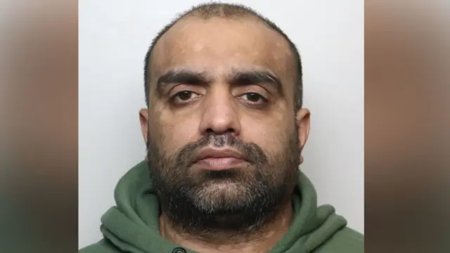 A man of about 40 with shaved hair wearing a green tracksuit. He is staring directly into the camera.