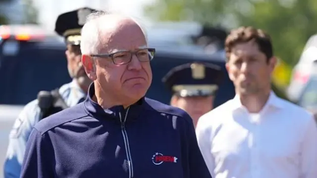 Tim Walz stands in front of Jacob Frey in August 2025