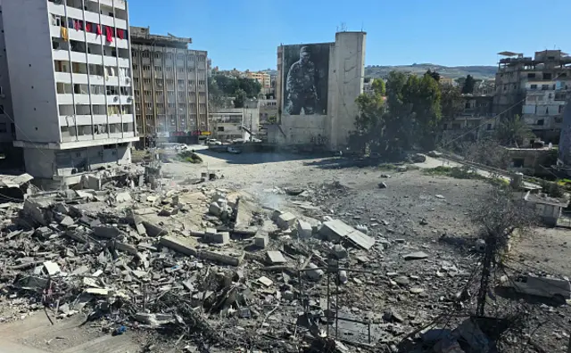 The rubble from a destroyed building is seen in a square in front of several tall blocks