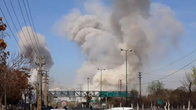 People run for safety as smoke rises after an airstrike in central Tehran, Iran