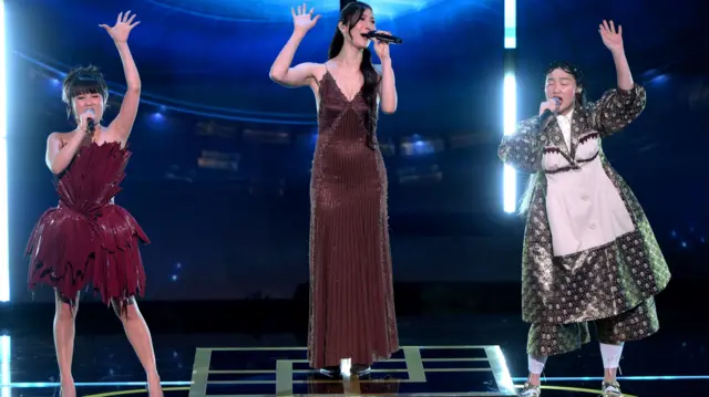 Rei Ami, EJAE and Audrey Nuna sing on stage with the arms in the air