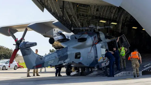 A British Wildcat helicopter being unloaded from the back of a C-17 airplane.